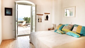 A bedroom with a large bed, a wooden ceiling, a glass door leading outside, and a small table with a lamp. - Upscale seaside villa, breathtaking view, near Naoussa and Santa Maria (NAOUSSA)