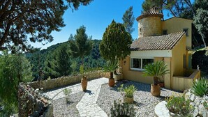 Een villa in mediterrane stijl met een stenen pad dat naar een geel gebouw leidt, omringd door plantenpotten en bomen.