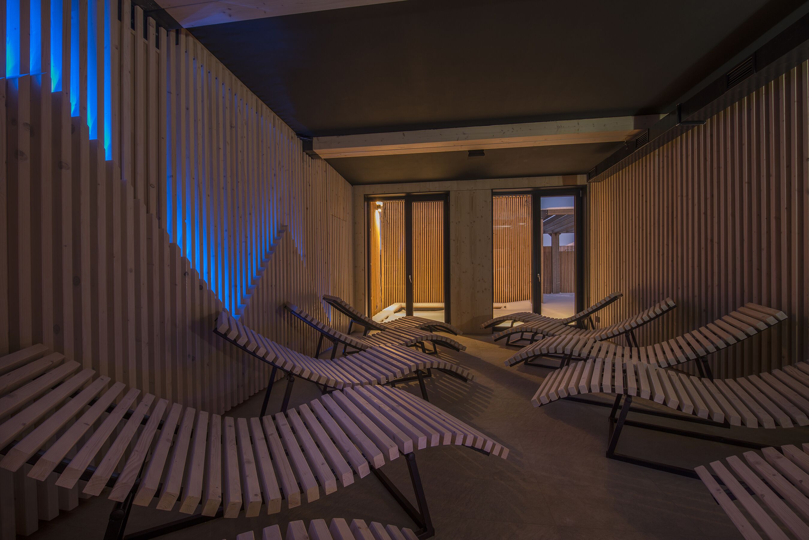 Un espace spa avec des murs recouverts de lambris en bois, plusieurs chaises longues et une vue sur l’extérieur.