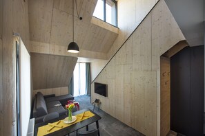 A modern interior with a sloped ceiling, a dining area with a table and chairs, a sofa, and a flat-screen TV mounted on the wall. - Demänová Rezort (Liptovsky Mikulas)
