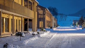 A snow-covered road leading to a building with large windows and a wooden facade.