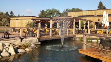 A restaurant with outdoor seating overlooking a pond with a fountain.