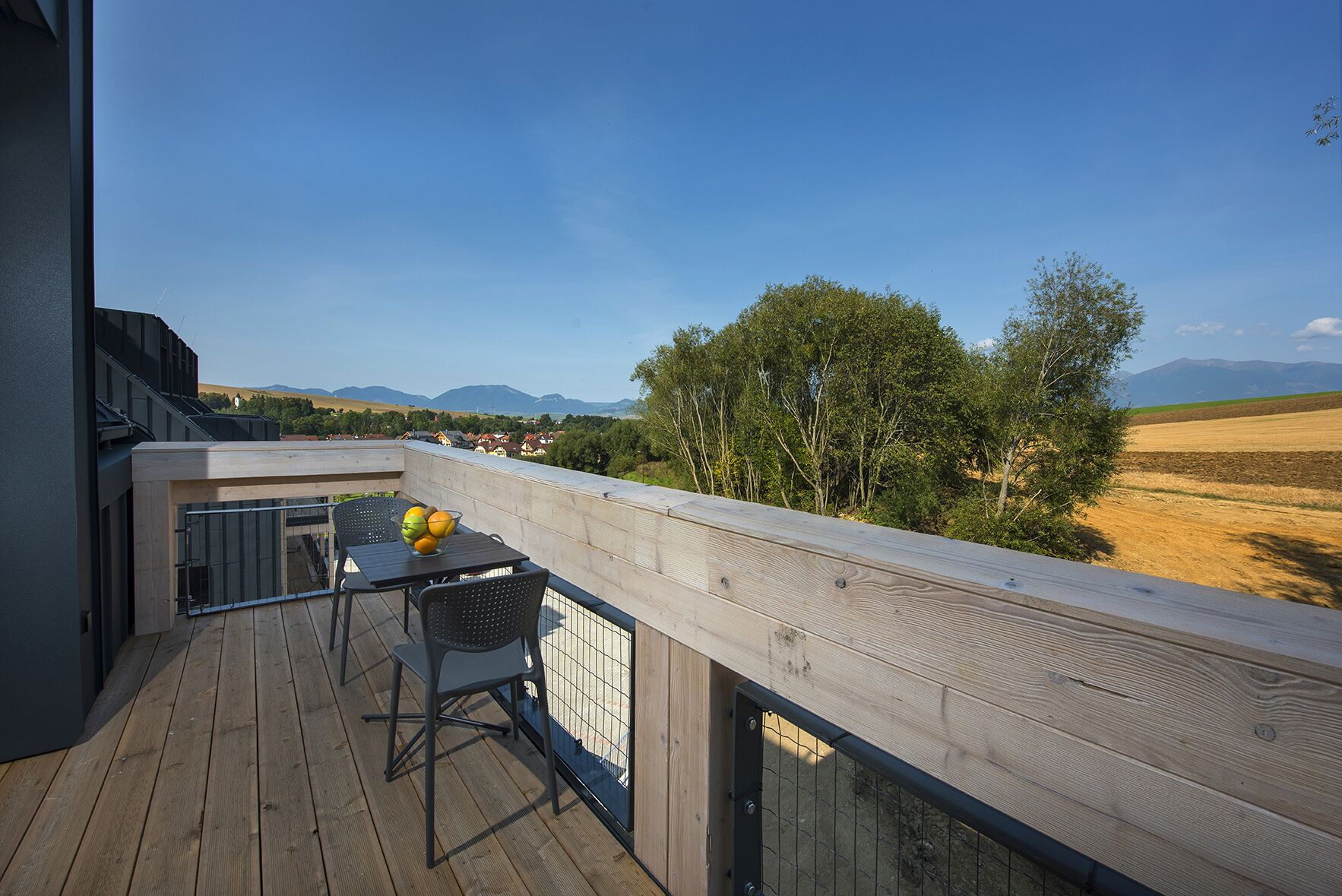 Ein Balkon mit Holzdeck, Metallgeländer und einem Tisch mit Obstschale.