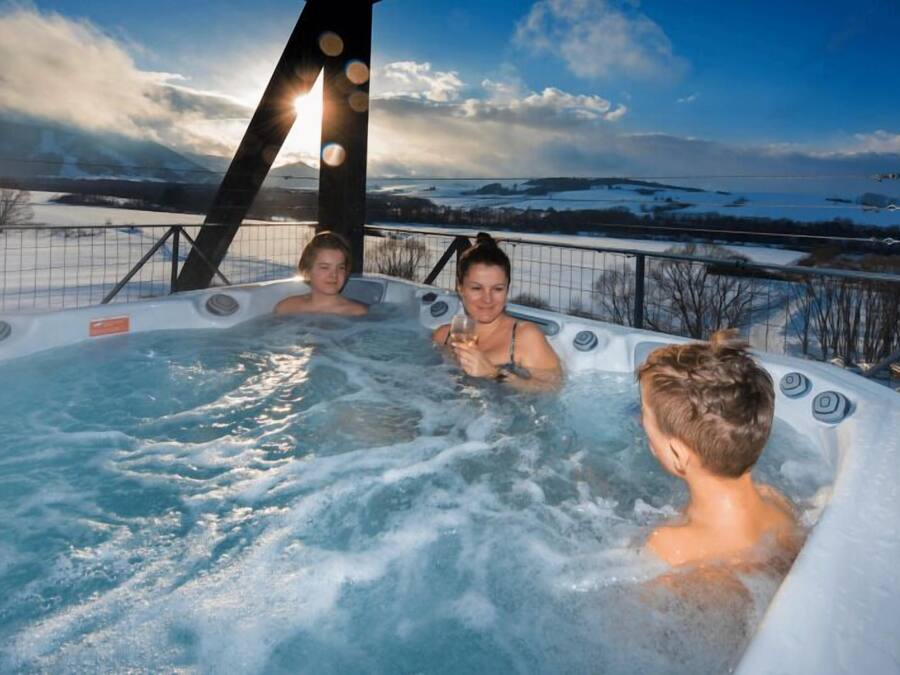 A hot tub with three people in it, surrounded by a snowy landscape and a clear sky.