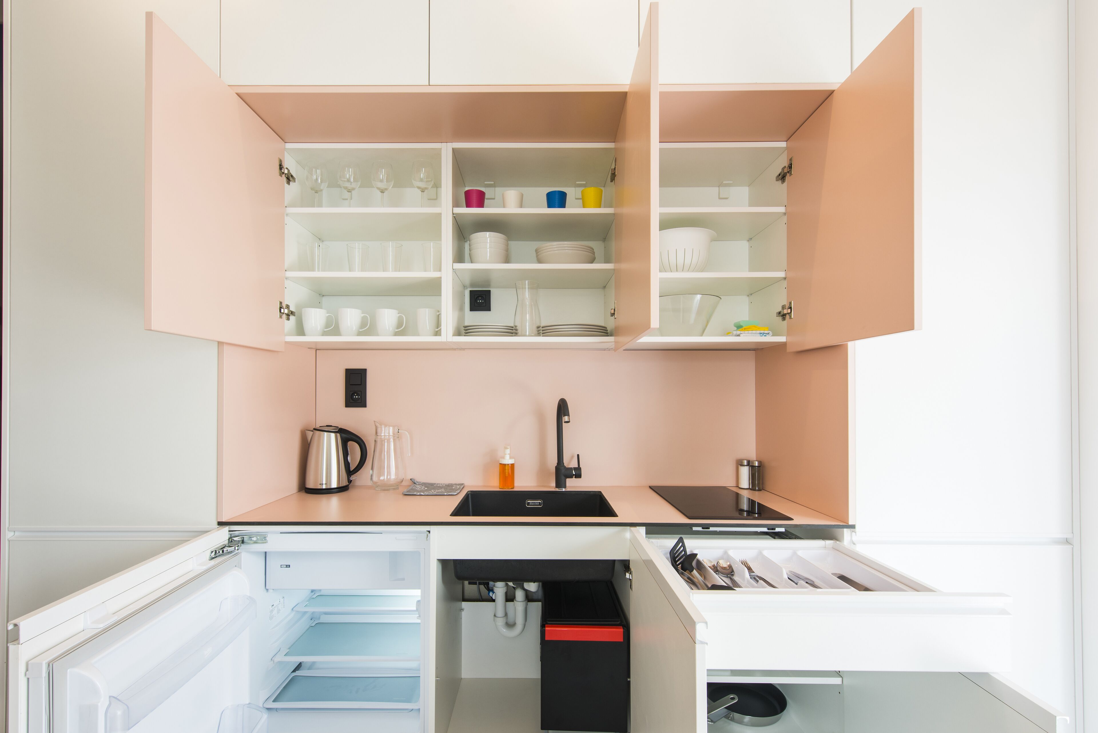 A compact kitchen with open cabinets, a sink, and a built-in refrigerator.