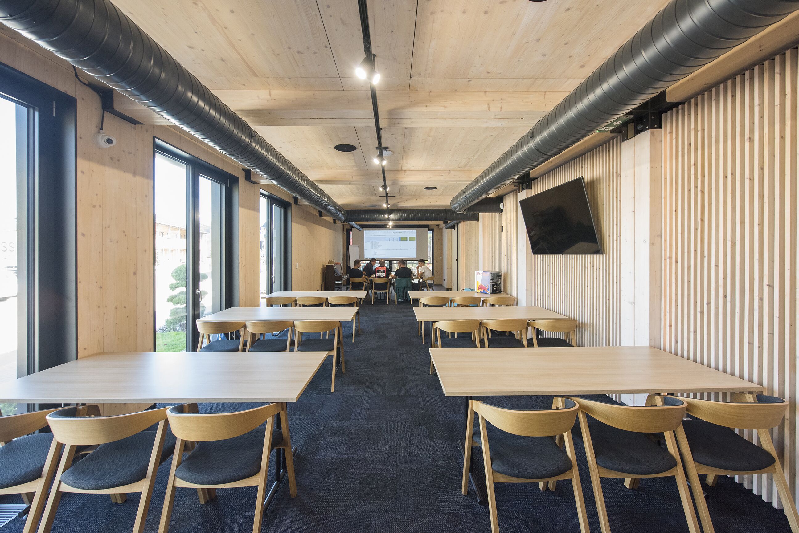 A conference room with long tables and chairs, a projector screen, and a large window.