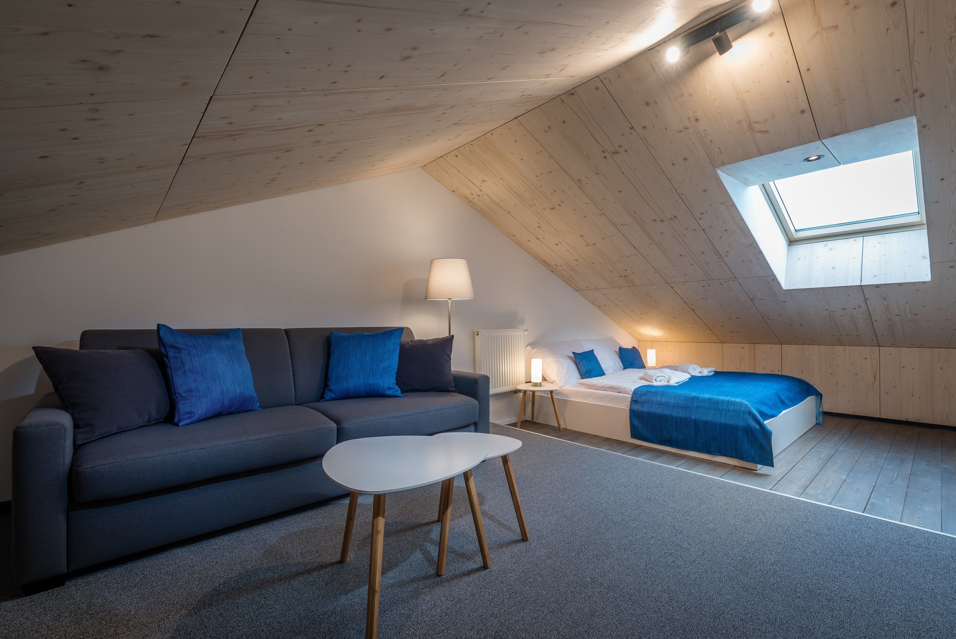 Un dormitorio tipo loft moderno con techo inclinado, tragaluces, sofá, cama y una mesita.