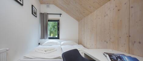 Un dormitorio con techo de madera, cama con ropa de cama blanca, escritorio con silla y ventana con cortinas.
