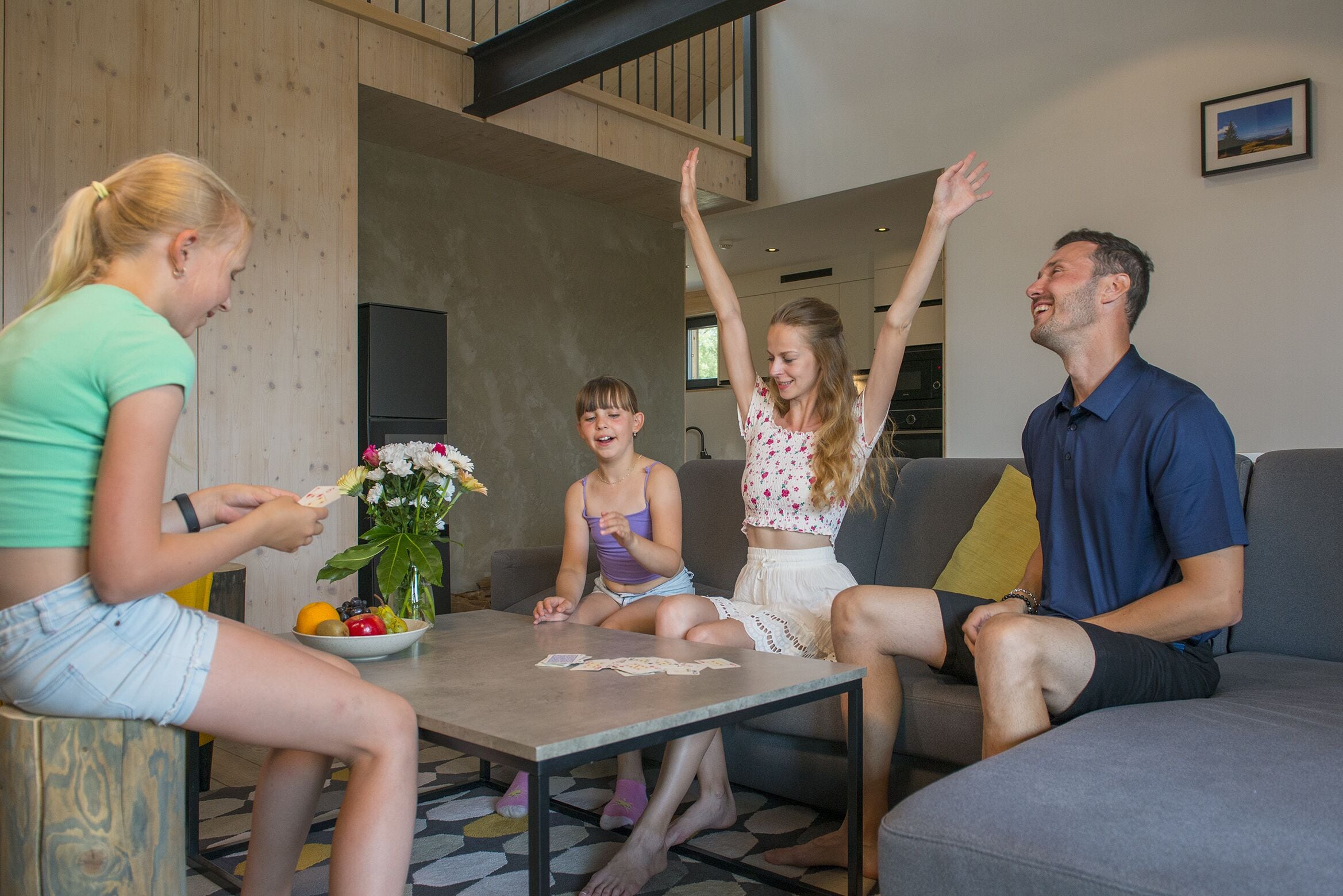 Uma família de quatro pessoas em uma sala de estar moderna, com um sofá, uma mesa de centro e um vaso de flores.