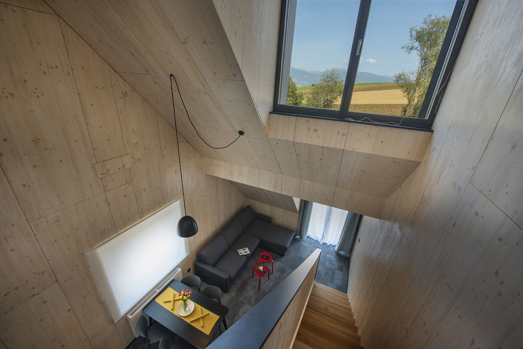 Un interior moderno con techo de madera, un sofá, una mesa de comedor y vista a un paisaje a través de un ventanal grande.