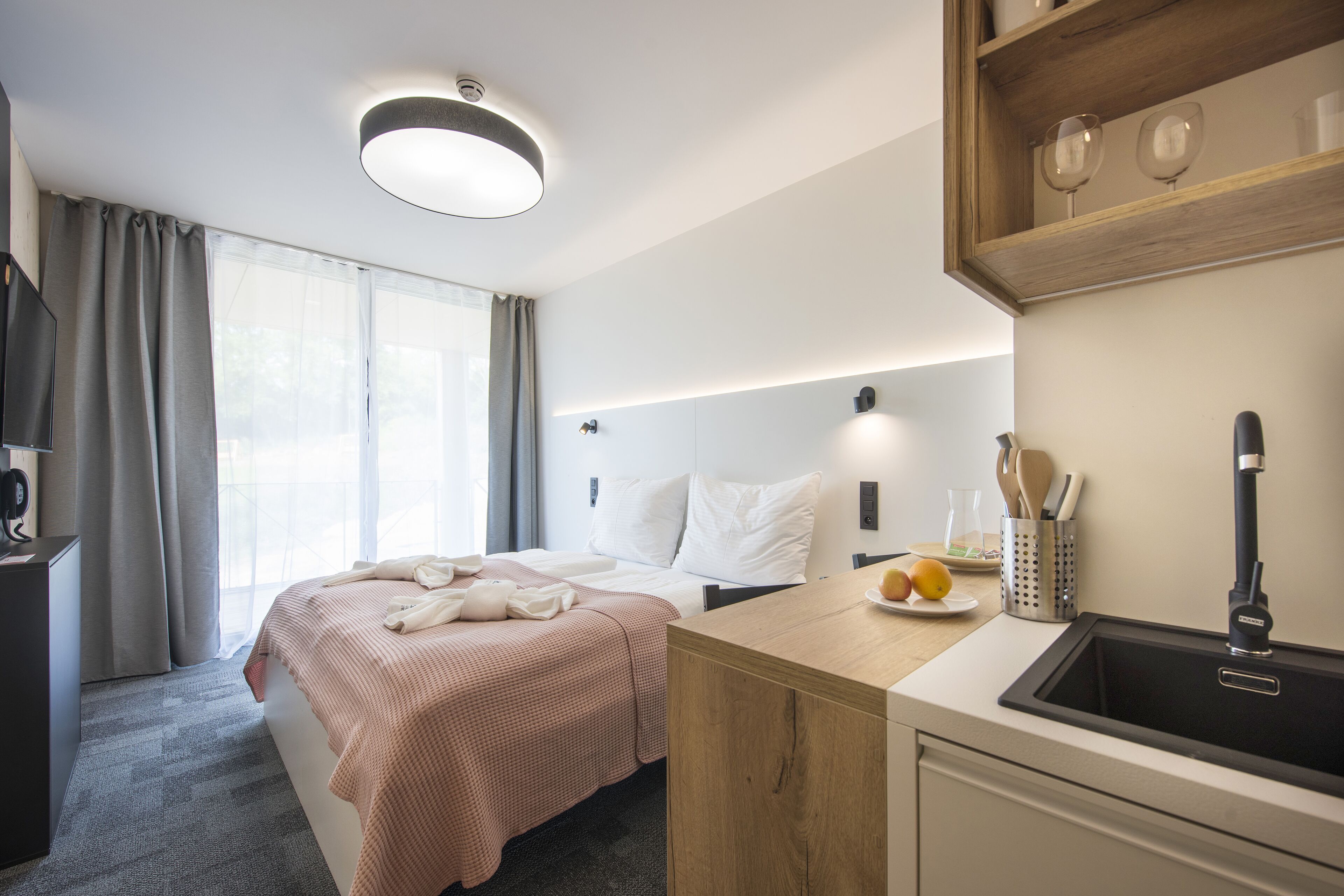 A hotel room with a bed, a desk with a sink, and a window with curtains.