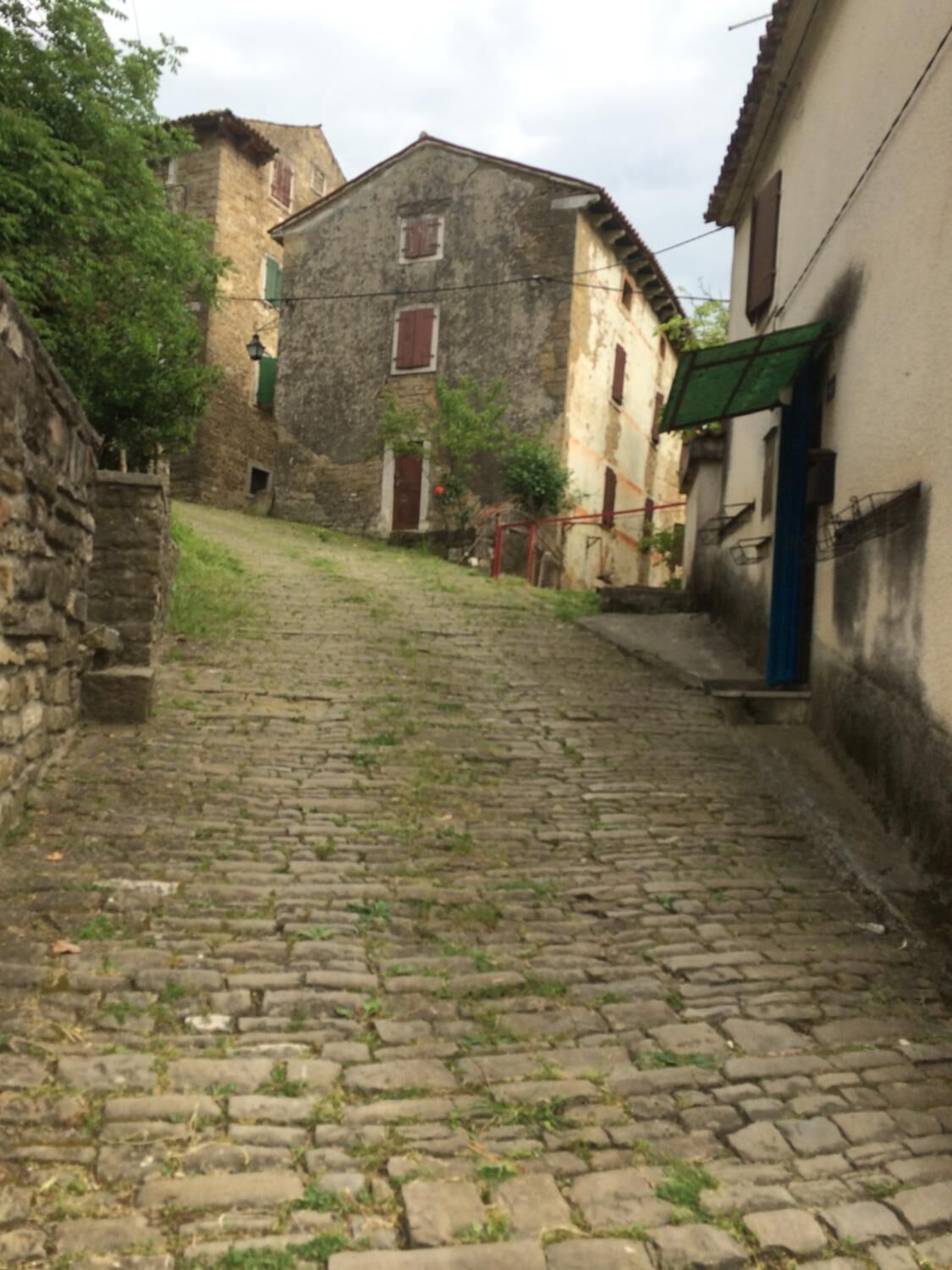 Eine gepflasterte Straße mit alten Gebäuden, einer Steinmauer und einem schmalen Gang.