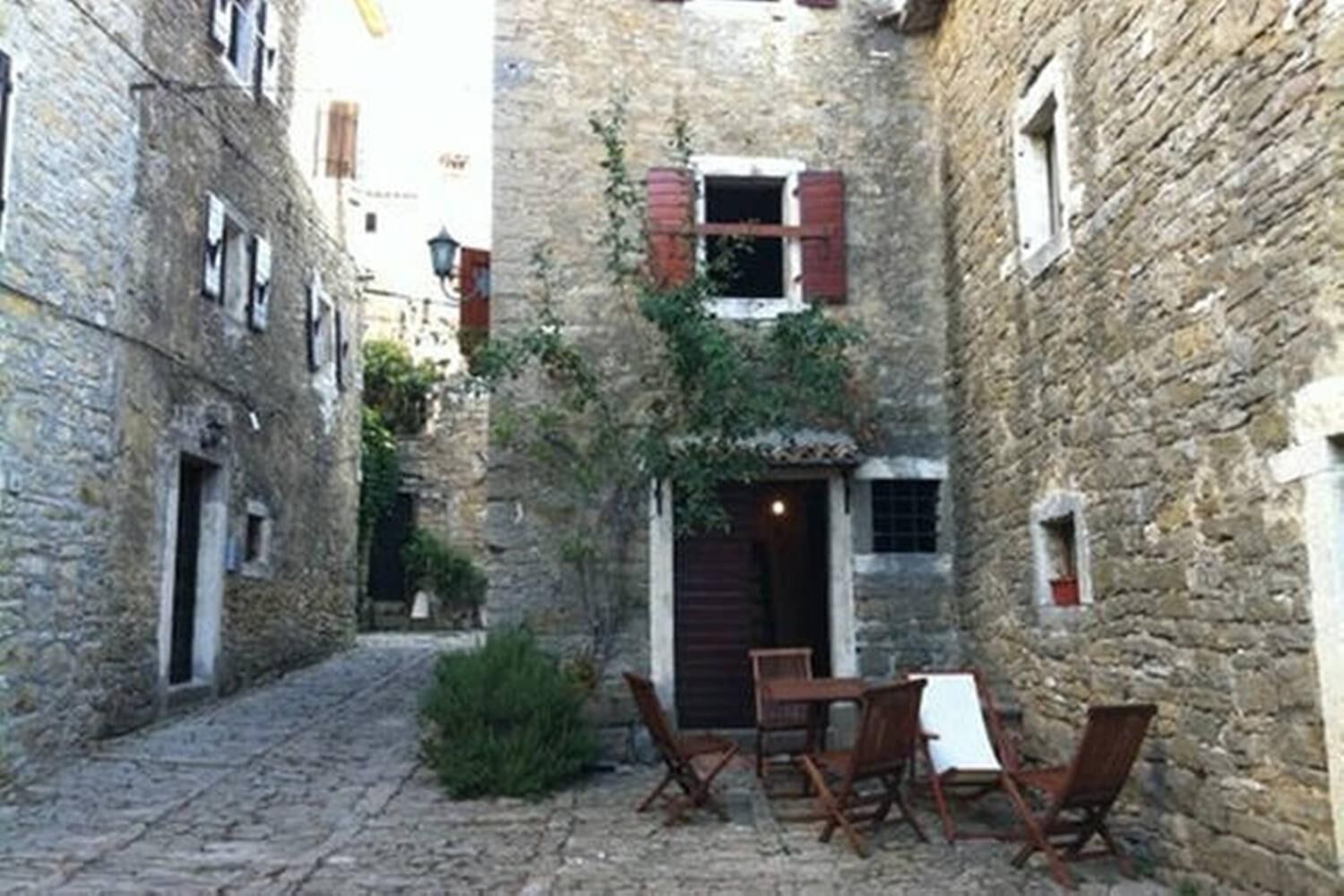 Un estrecho callejón adoquinado con edificios de piedra, una mesa de madera y sillas en el centro.