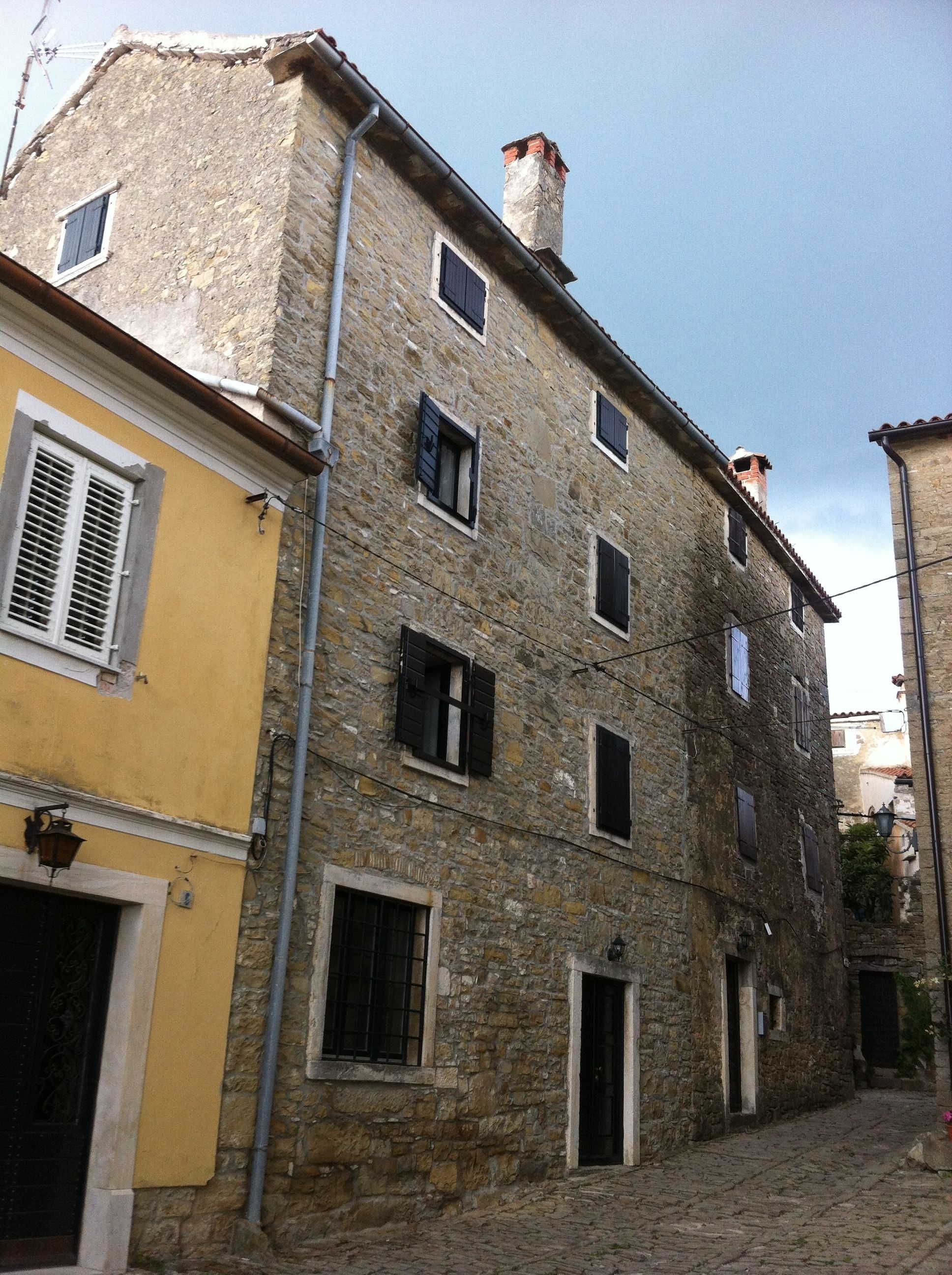Un bâtiment en pierre doté de nombreuses fenêtres et d’une porte, donnant sur une rue pavée.