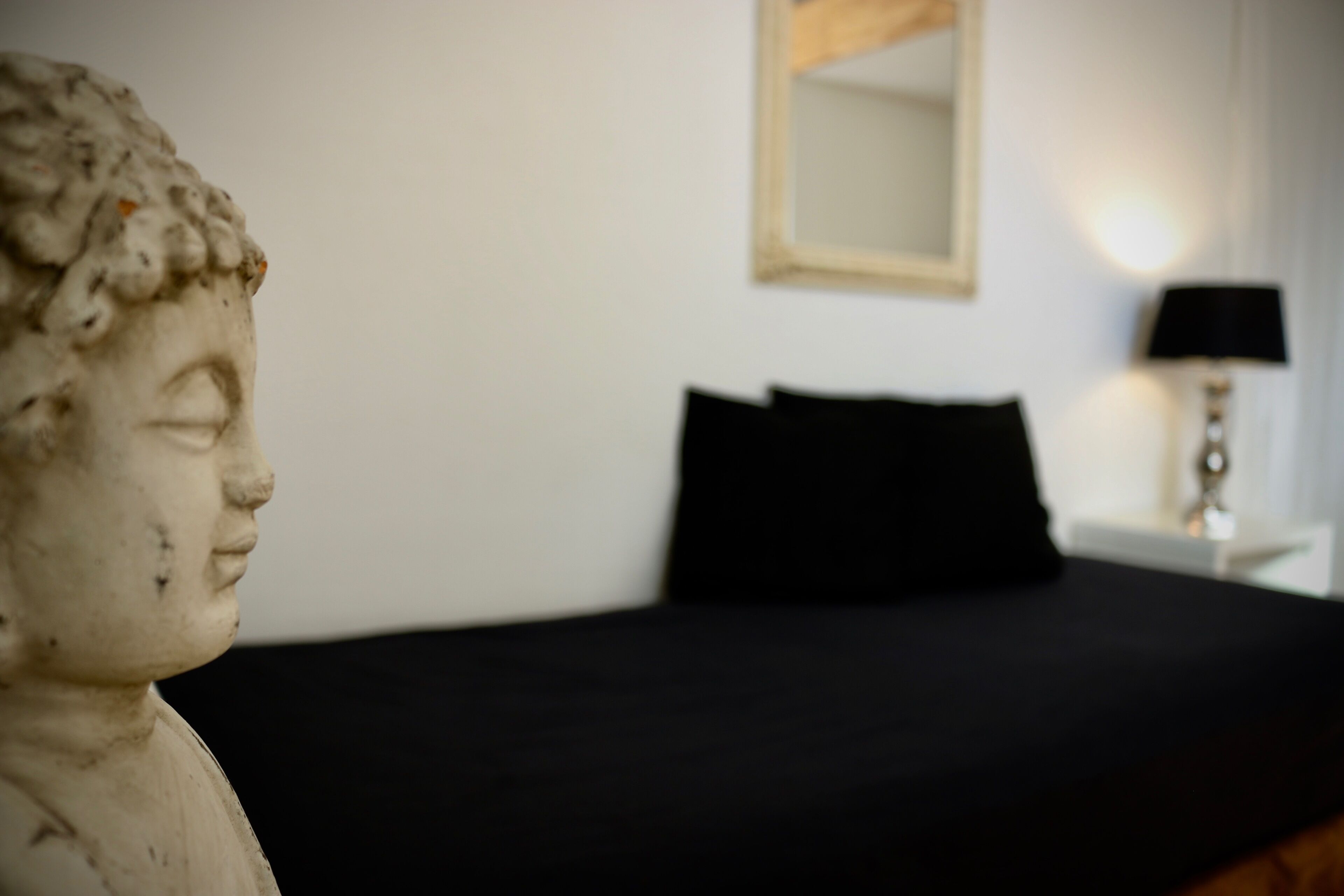 Eine Statue in einem Zimmer mit einem Bett, einem Nachttisch und einer Lampe.