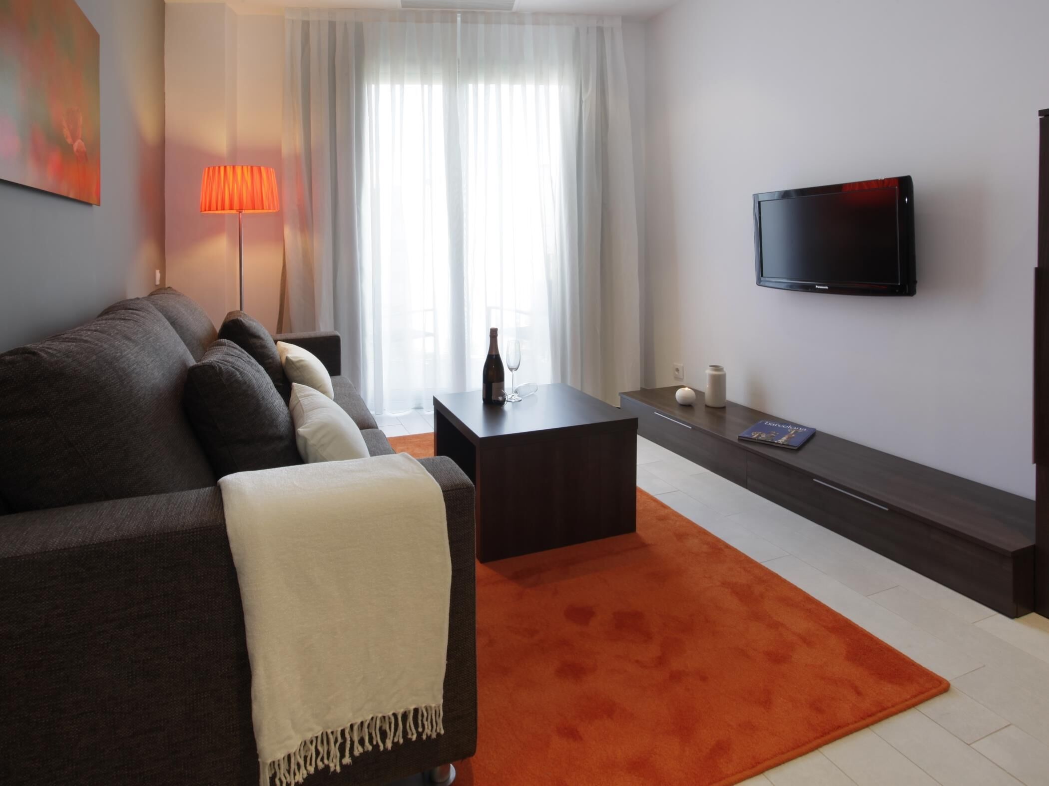 A modern living room with a sofa, a coffee table, a TV, and a window with curtains.