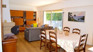 A dining area with a table set for four, surrounded by wooden chairs. A kitchen with wooden cabinets and a built-in oven is visible in the background. - Very nice renovated family house (DINAN)