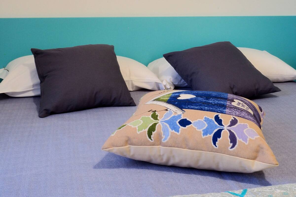 A bed with a teal headboard, two dark pillows, and a decorative pillow with a floral pattern.