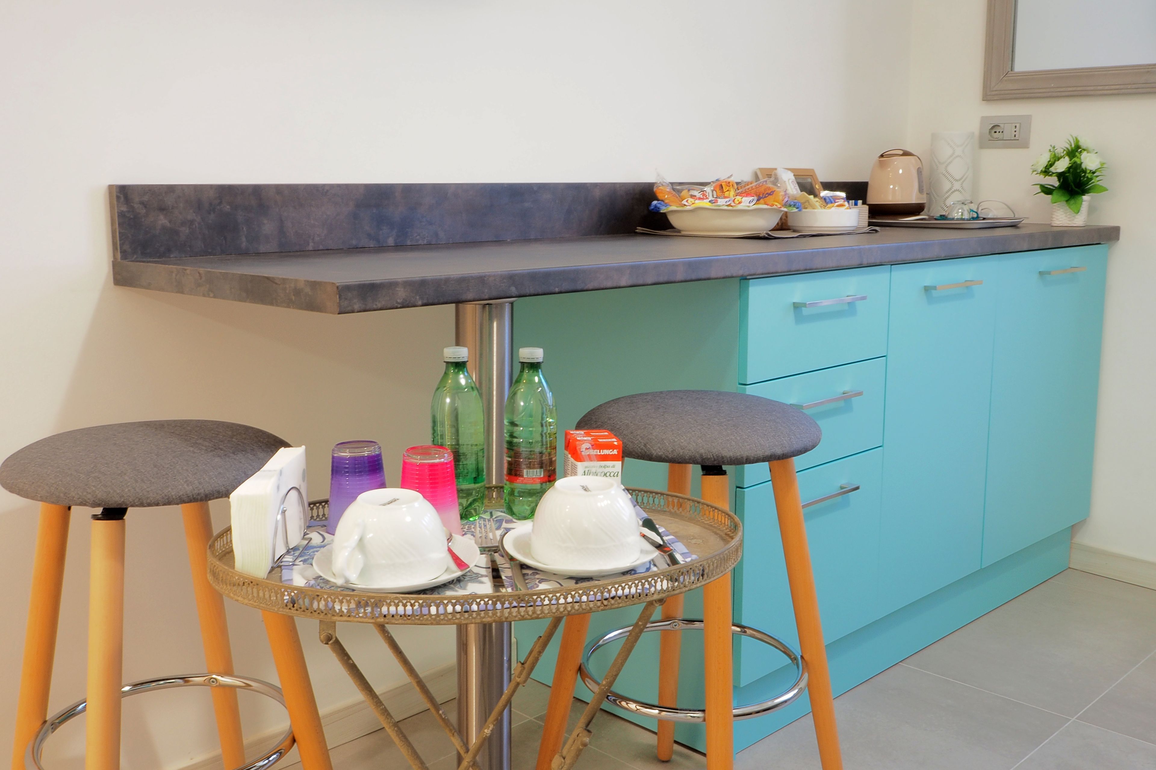 Un coin cuisine comprenant un tabouret de bar, un évier et un plan de travail sur lequel sont disposés divers objets.