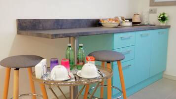 Un coin cuisine comprenant un tabouret de bar, un évier et un plan de travail sur lequel sont disposés divers objets.