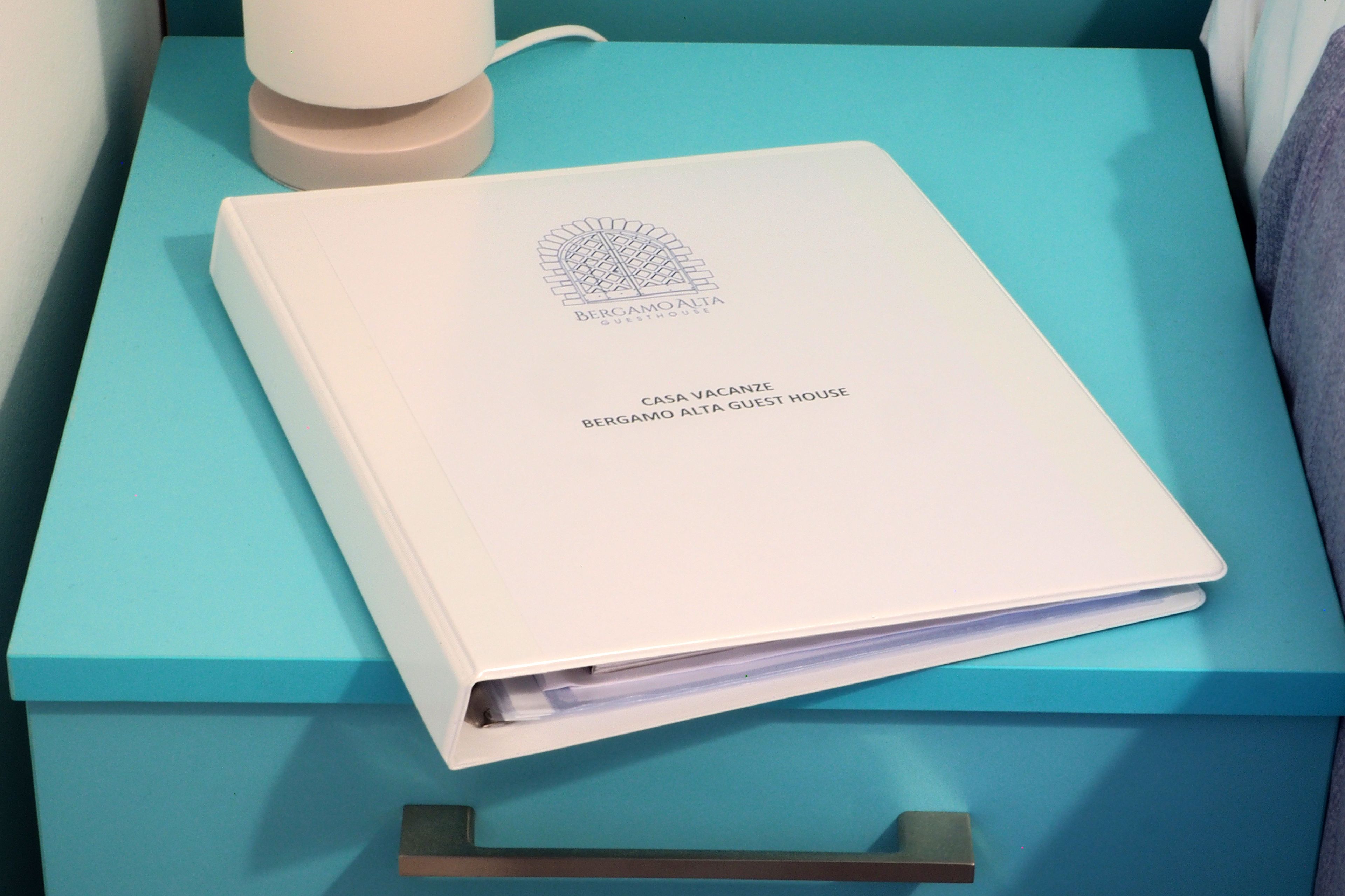 A white booklet titled "Bergamo Alta Guest House" on a teal-colored surface.