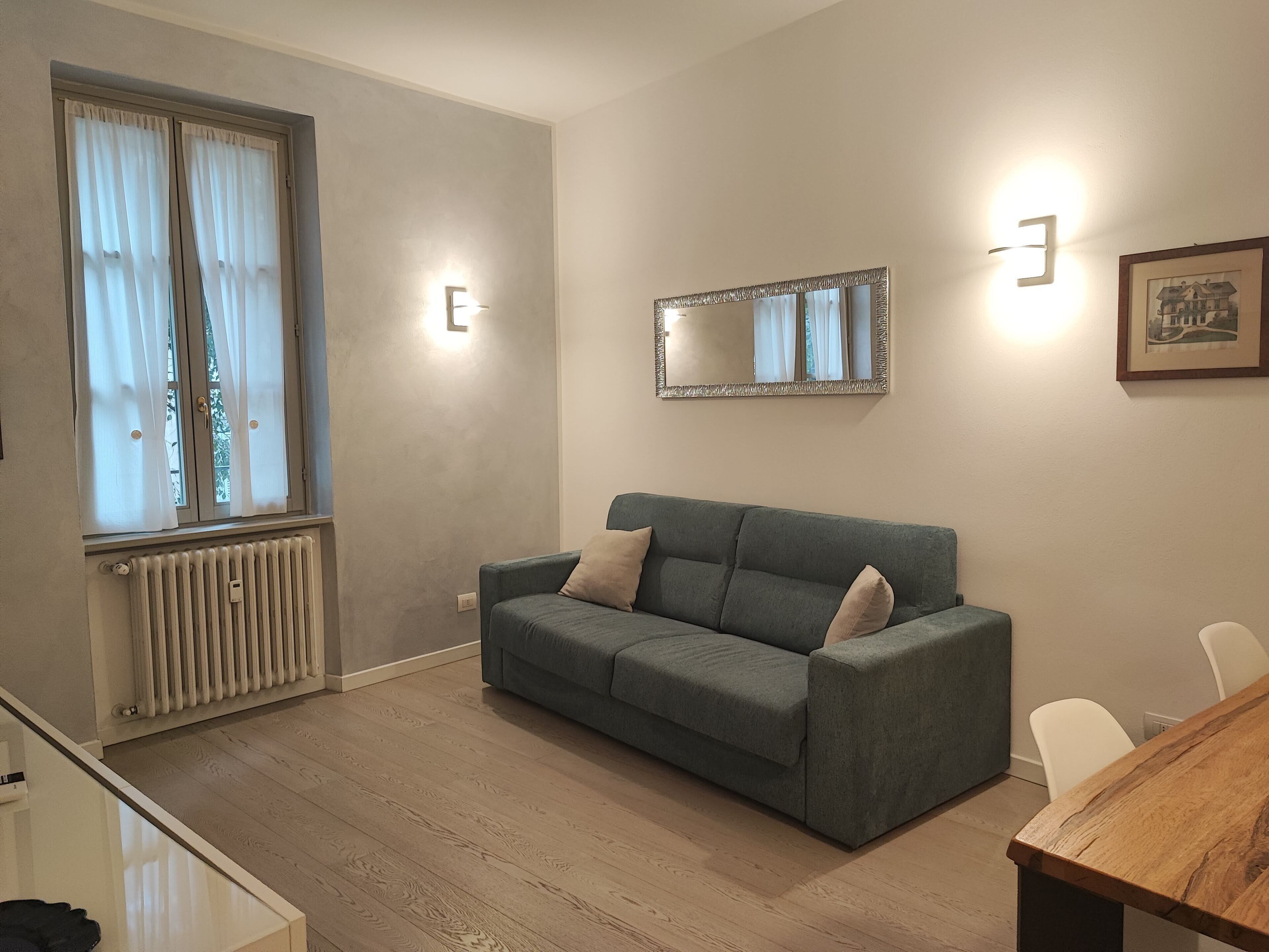 A modern living room with a grey sofa, a wooden dining table, and a radiator.