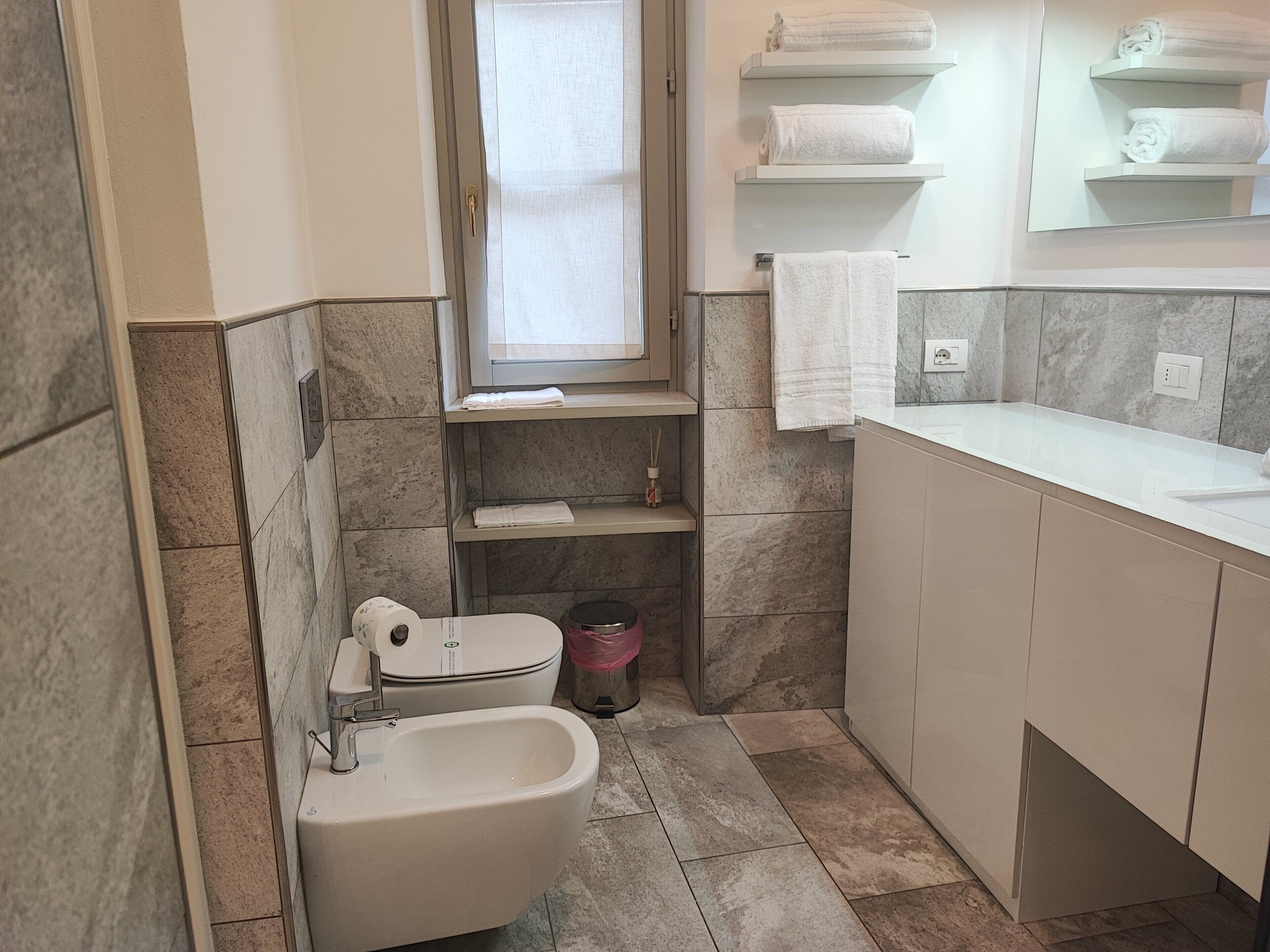 Une petite salle de bain comprenant des toilettes, un bidet et des étagères pour les serviettes.