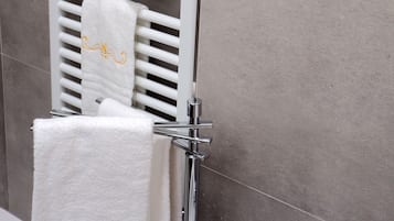 A bathroom with a white towel rack holding three towels, a chrome faucet, and a white sink.