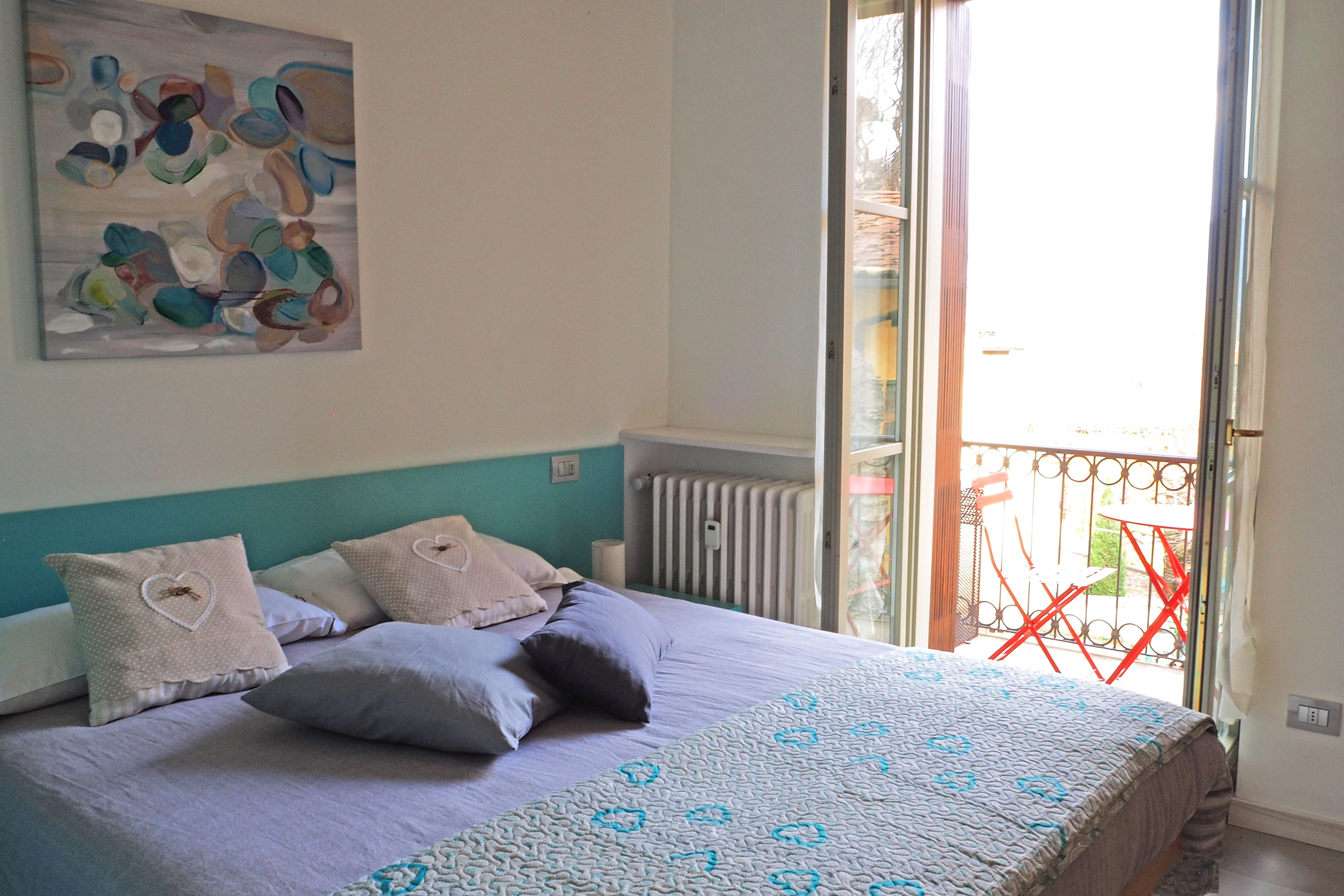 A bedroom with a bed, pillows, a wall art piece, and a balcony with a red chair.