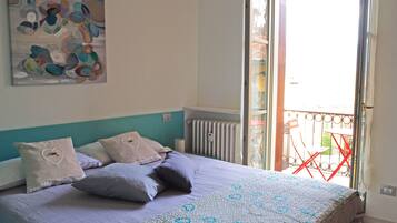 A bedroom with a bed, pillows, a wall art piece, and a balcony with a red chair.