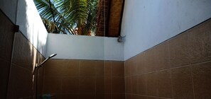 A bathroom with brown tiles, a shower, and a view of palm trees.