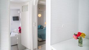 A hotel room with a bed, a bedside table, a lamp, and a vase with flowers. - Chora House (Mykonos)
