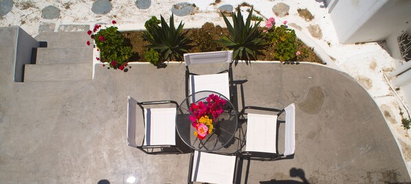 A patio with a table and two chairs, surrounded by plants and flowers. - Chora House (Mykonos)