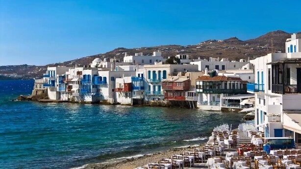 A coastal town with white buildings with blue accents, a clear blue sea, and a rocky shoreline. - Chora House (Mykonos)