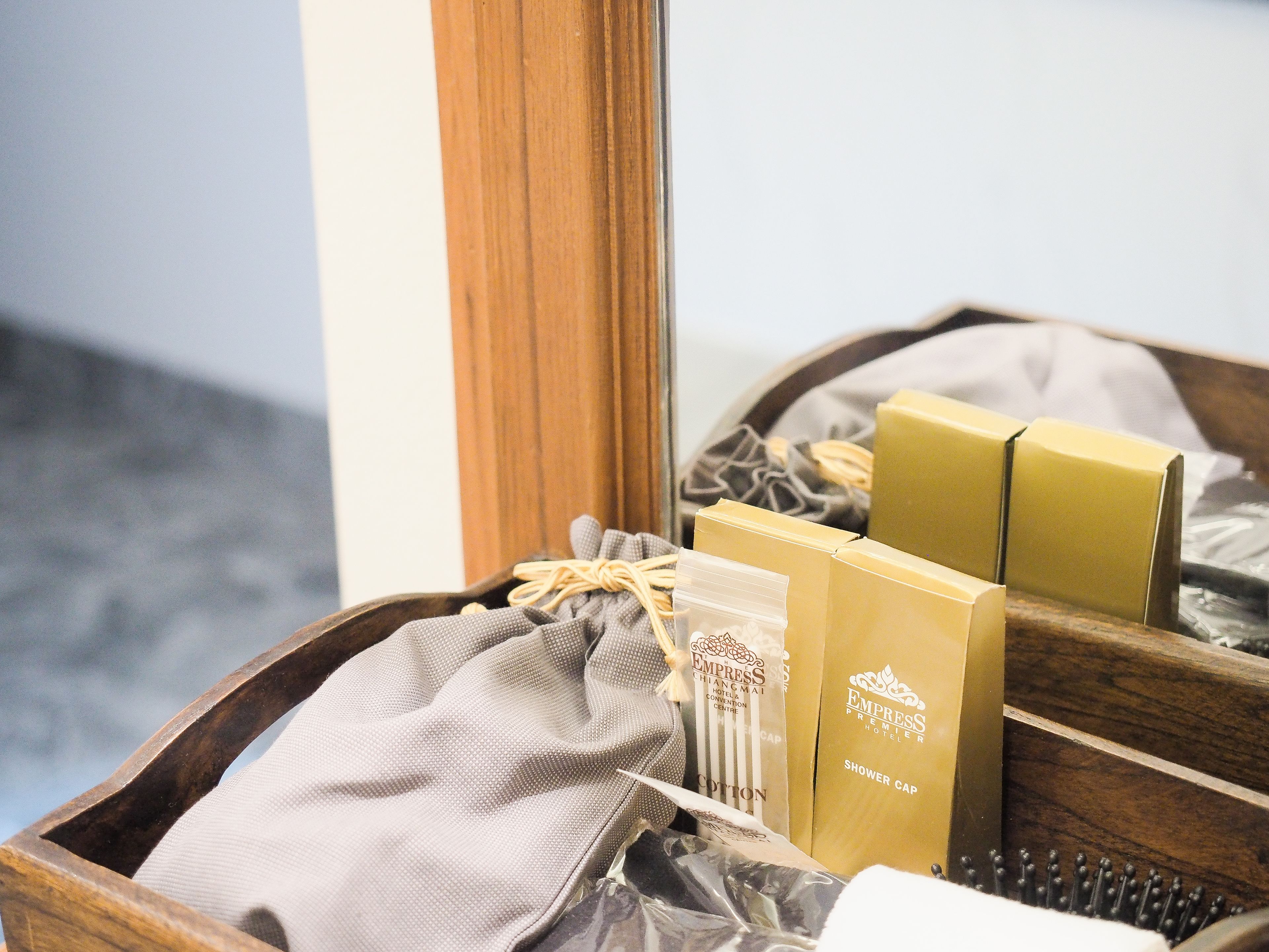 A wooden tray with a grey cloth, a cotton bag, and two shower cap boxes labeled "Empress Premier Hotel".