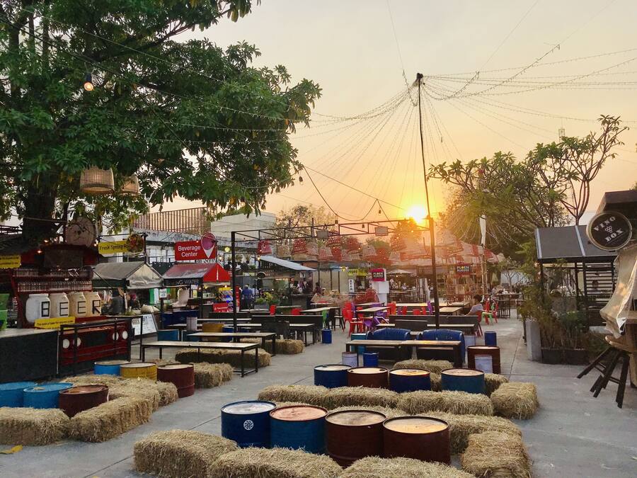 An outdoor market with tables, hay bales, barrels, and various stalls.
