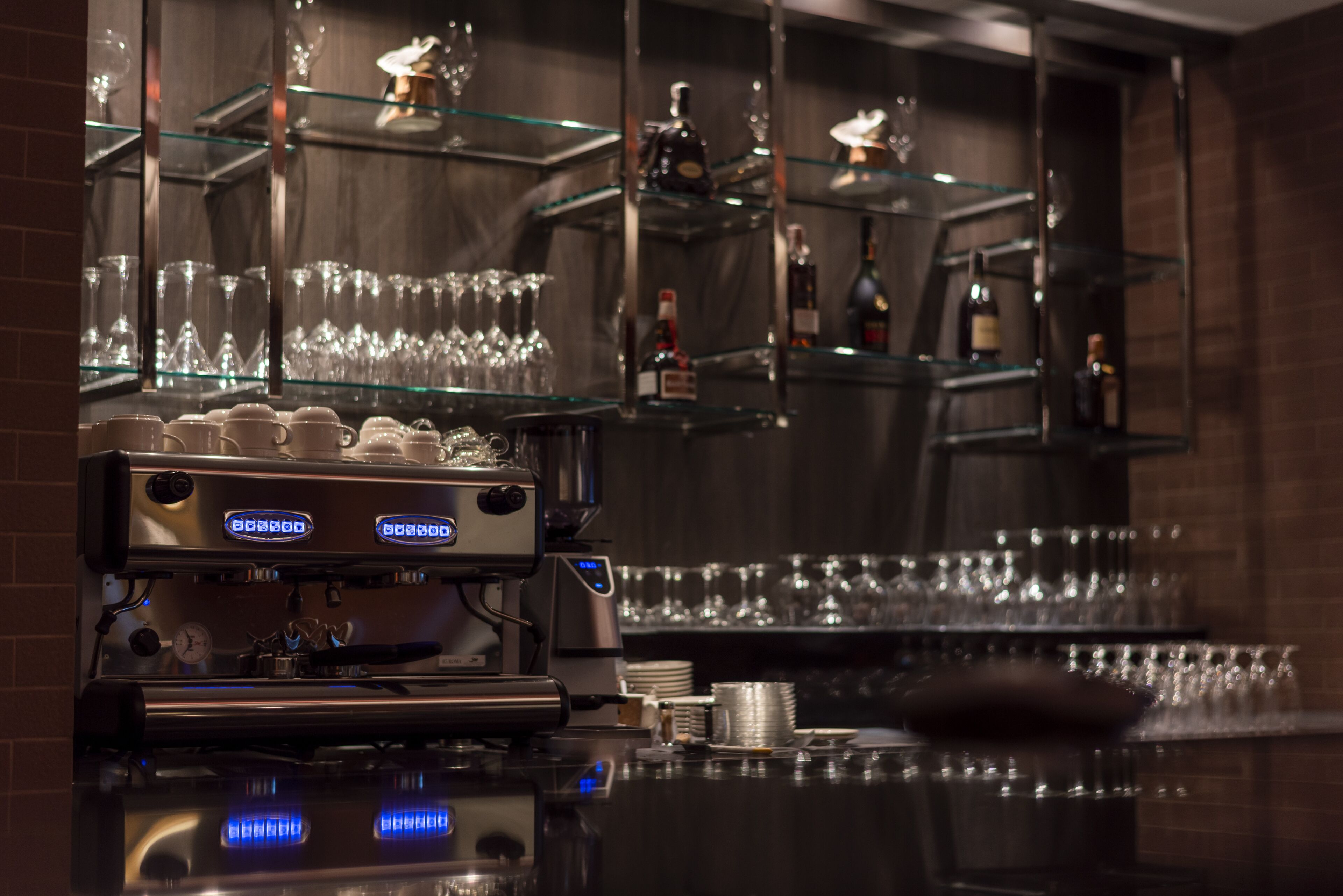 Una zona de bar con una máquina de café, estanterías con vasos y botellas.