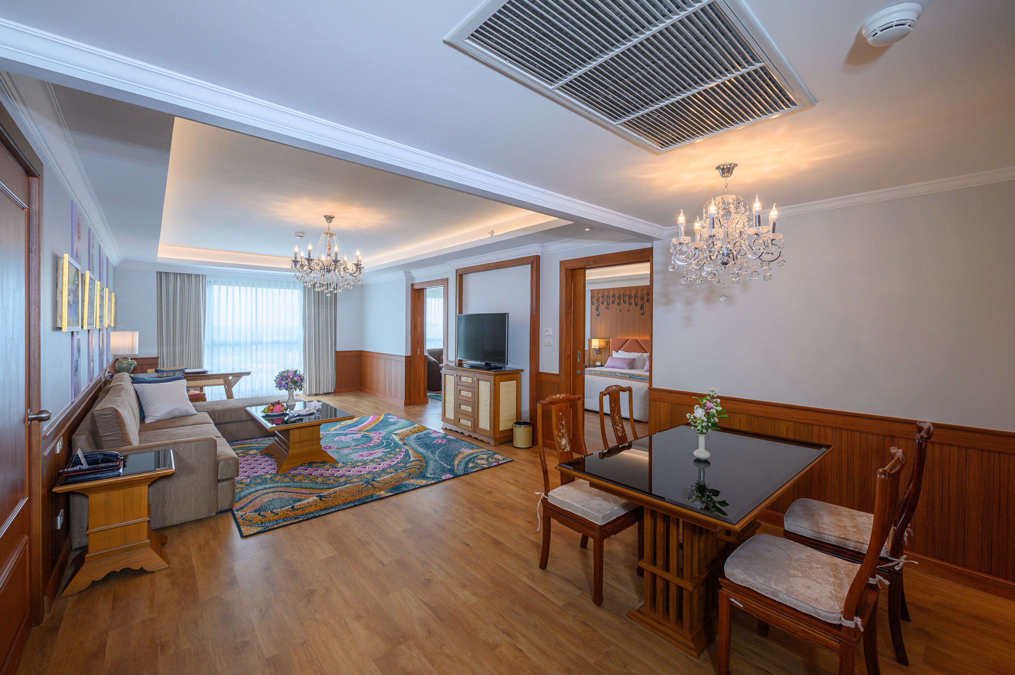 A spacious living room with a sofa set, a dining table with chairs, a television, and a large window.