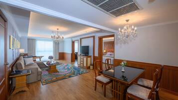 A spacious living room with a sofa set, a dining table with chairs, a television, and a large window.