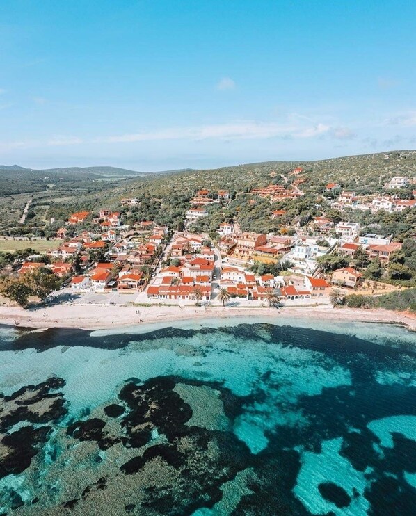 Ein Luftbild einer Küstenstadt mit roten Dächern, einem Strand und klarem türkisblauem Wasser.