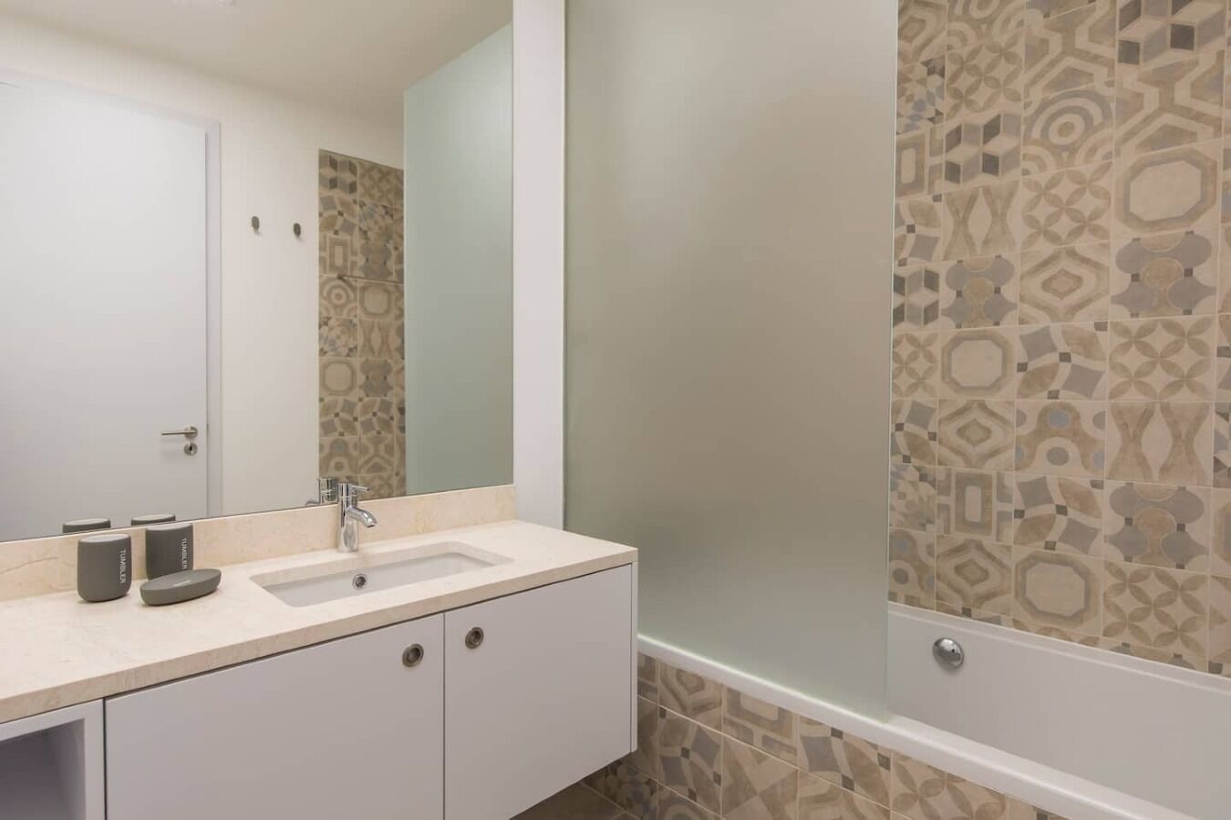 A bathroom with a white sink, a mirror, and patterned tiles on the walls.