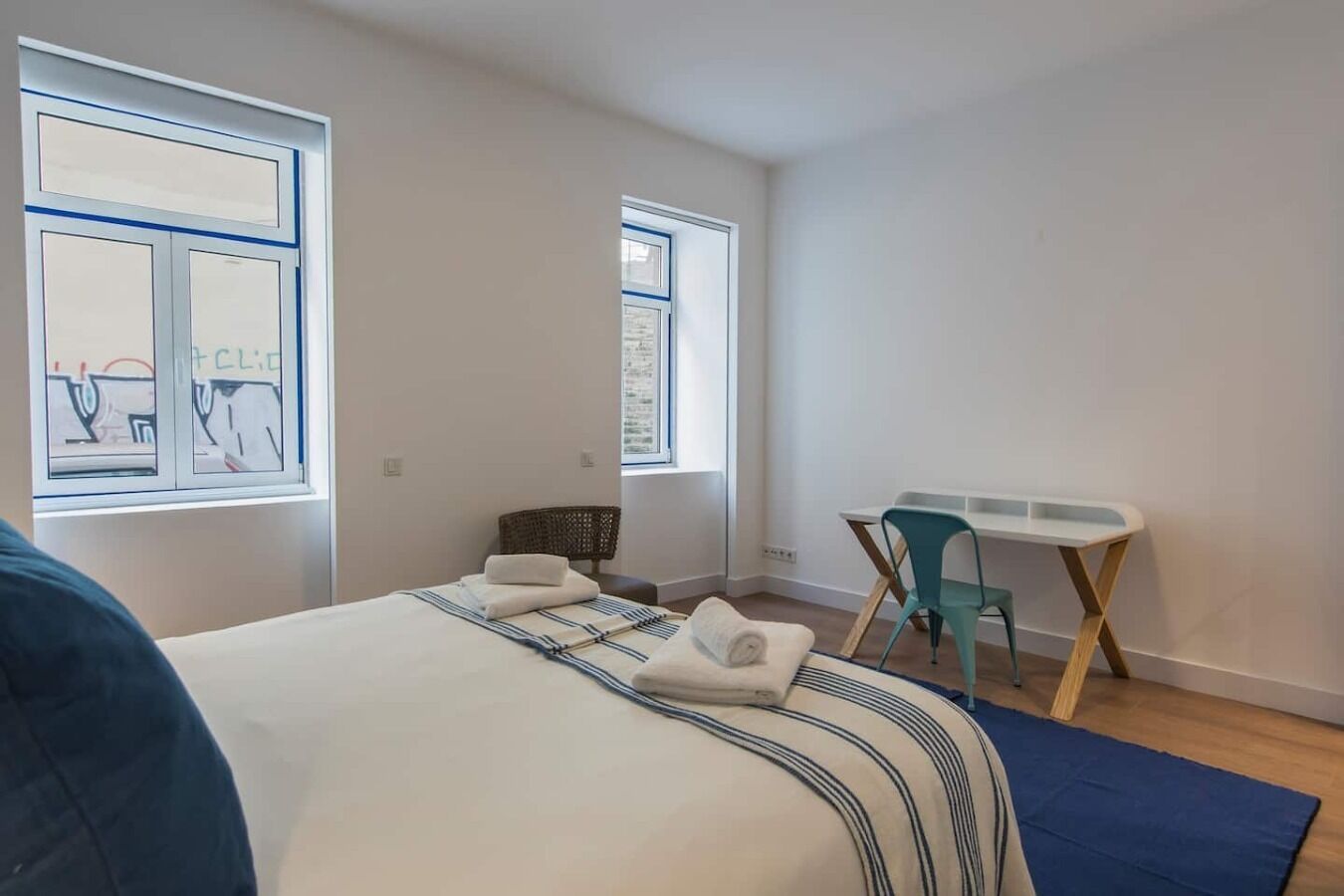 A bedroom with a bed, a desk, and two windows.