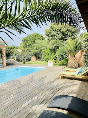 A wooden deck with a pool, lounge chairs, and lush greenery. - DETACHED UPSTAIRS VILLA WITH PRIVATE POOL AND GARDEN (Porto Vecchio)