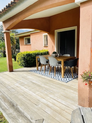 A covered patio area with a wooden table and chairs, a patterned rug, and a potted plant. - DETACHED UPSTAIRS VILLA WITH PRIVATE POOL AND GARDEN (Porto Vecchio)