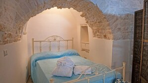 Een slaapkamer met een stenen boog, een bed met een blauwe sprei en een houten nachtkastje.