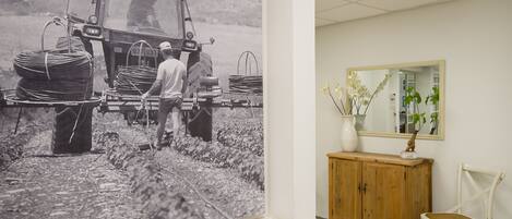 Una habitación con una amplia fotografía blanco y negro de un tractor y trabajadores, un aparador de madera, un espejo y una silla blanca.