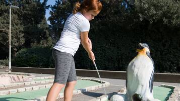 A person playing mini-golf with a penguin-shaped hole.