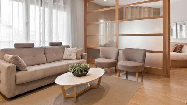 A modern living room with a sofa, two armchairs, a coffee table, and a large window with sheer curtains.