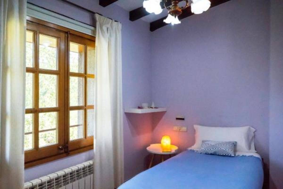 Une chambre à coucher avec un lit, une table de chevet avec une lampe, une fenêtre avec des rideaux et un radiateur.