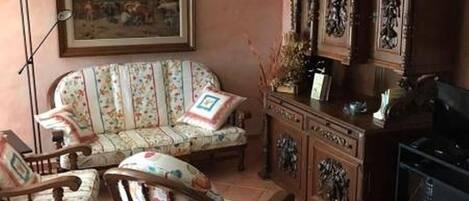 A room with a sofa, chairs, a cabinet, and a painting on the wall.